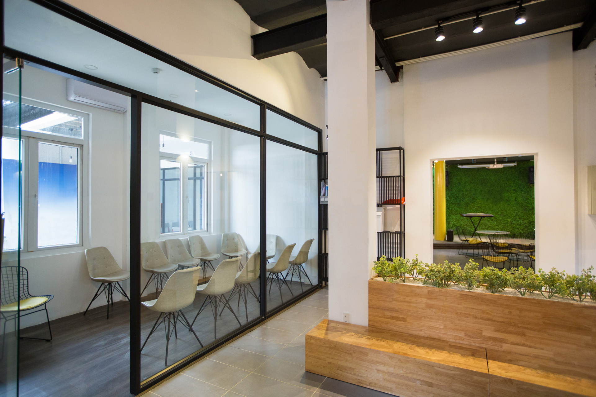 Nobody in office lobby with wooden bench. White wall with column and shelves. Green plants as part of interior. Many chairs behind glassy wall. Business center concept
